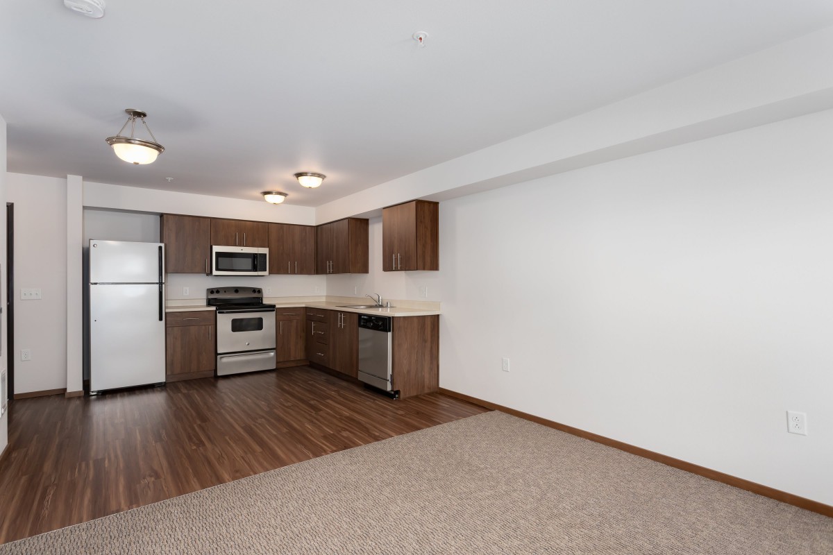 Modern apartment kitchen with wooden cabinets and stainless steel appliances.