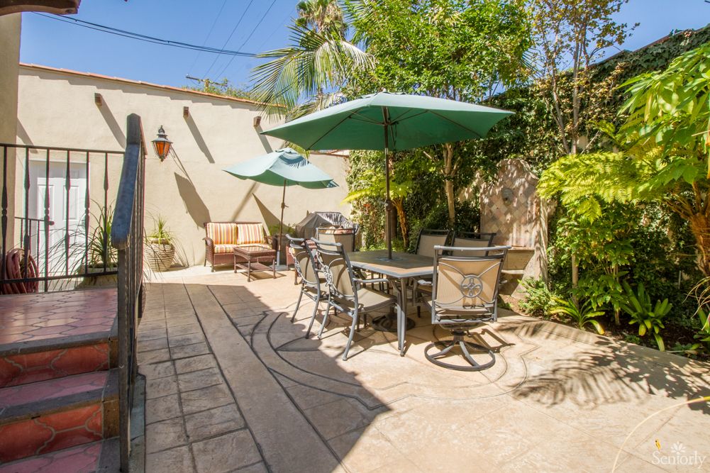 A sunny patio with outdoor furniture and umbrellas, surrounded by lush plants.