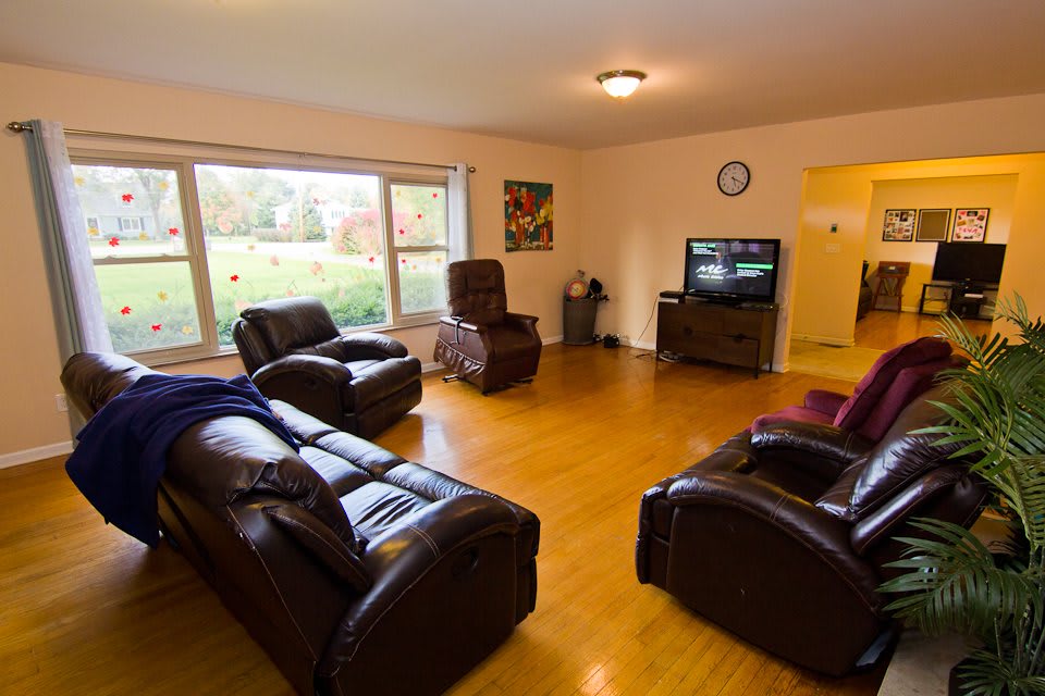 A cozy living room with leather sofas and a TV, featuring large windows that let in natural light.