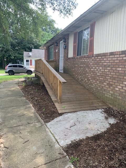 A wooden accessibility ramp leading to the entrance of a brick house.