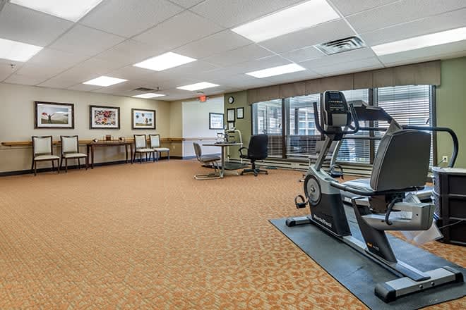 A spacious office area featuring exercise equipment, desks, chairs, and artwork on the walls.