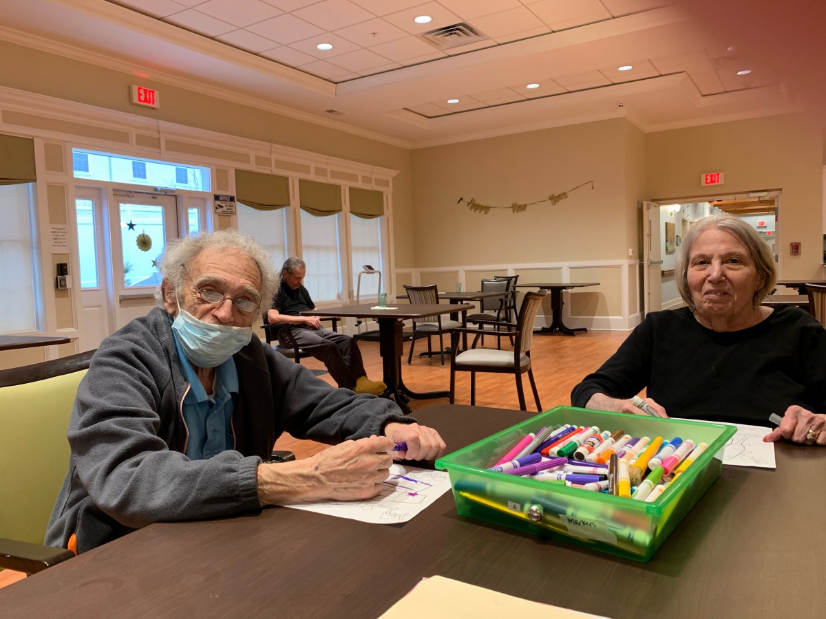 Two elderly individuals participate in a creative activity at a community center.
