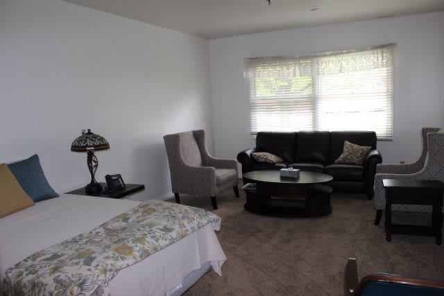 A cozy living room with a sofa, armchair, table, and lamp near a large window.