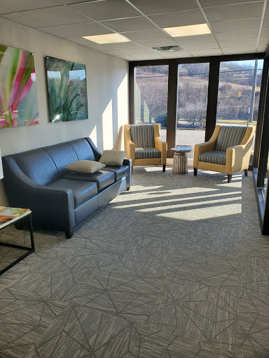 A cozy and well-lit office waiting area featuring a gray sofa and yellow armchairs.