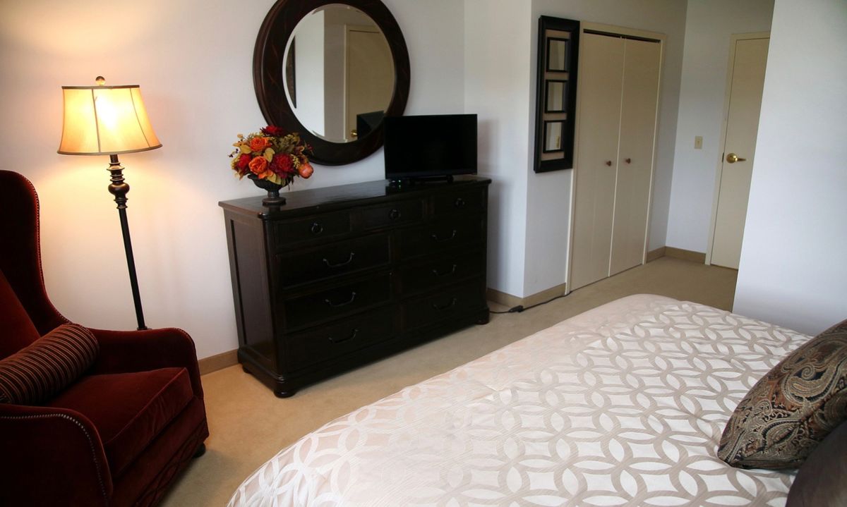 A cozy bedroom with a dresser topped by a round mirror, a television, and decorative flowers.