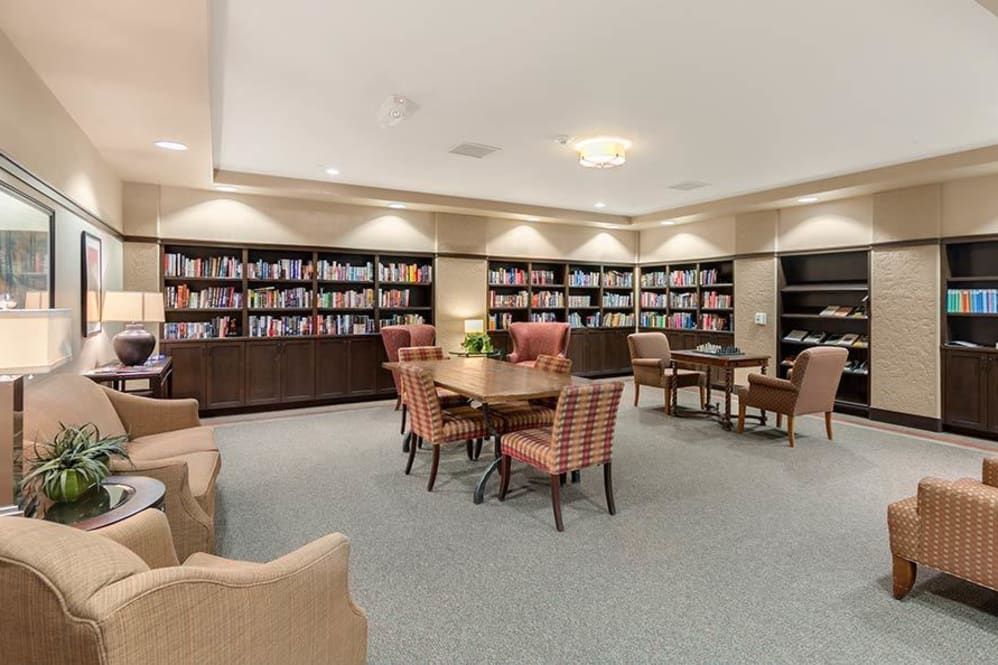 A cozy library reading area with bookshelves, comfortable chairs, and tables.