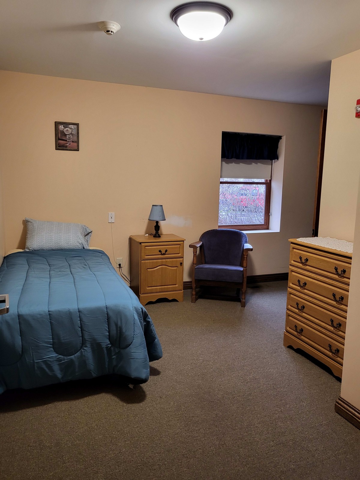 A cozy bedroom with a single bed, dresser, and armchair.