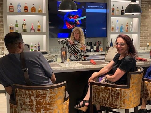 People enjoying drinks at a bar with a bartender serving and a TV in the background.
