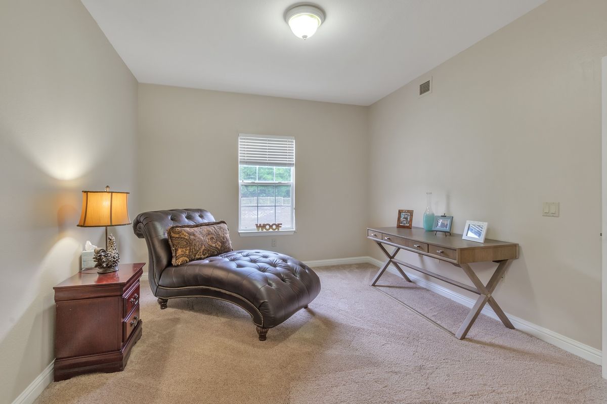A cozy room with a chaise lounge, desk, and lamp under soft lighting.