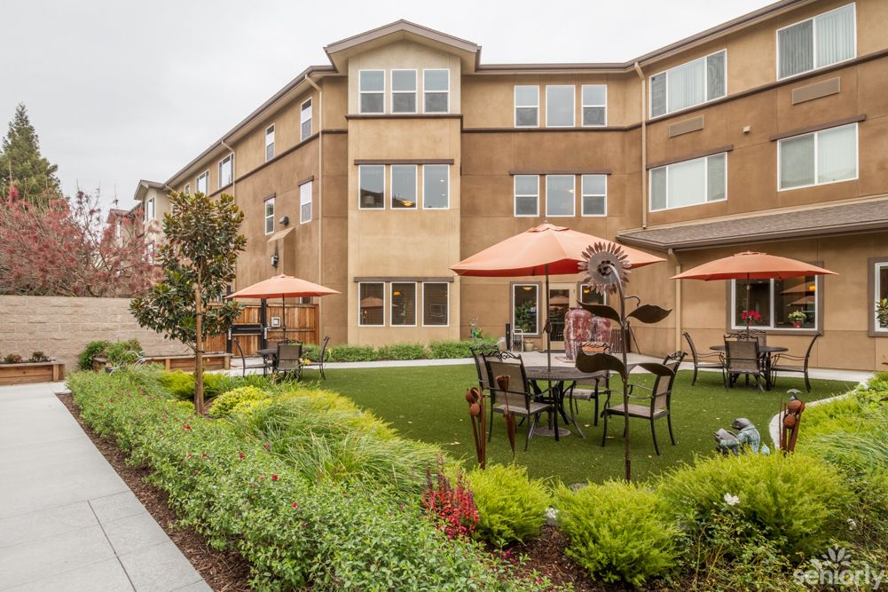 A well-maintained garden area with outdoor furniture and umbrellas in front of a modern residential building.