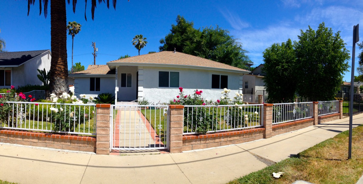 A suburban home with a garden and white fence on a sunny day.