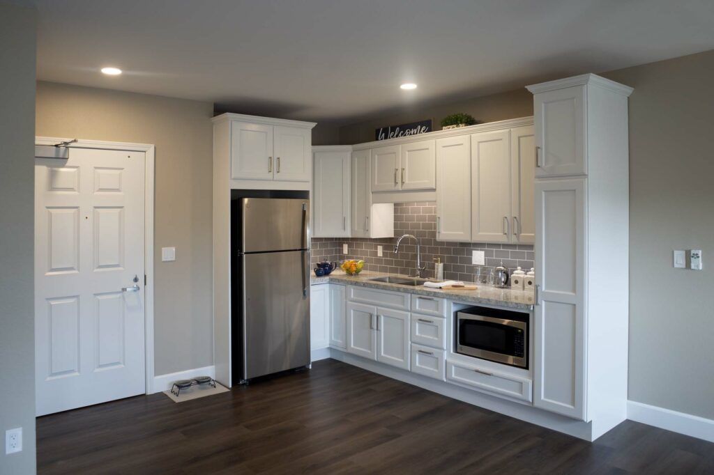 A modern kitchen with white cabinetry, stainless steel appliances, and wood flooring.
