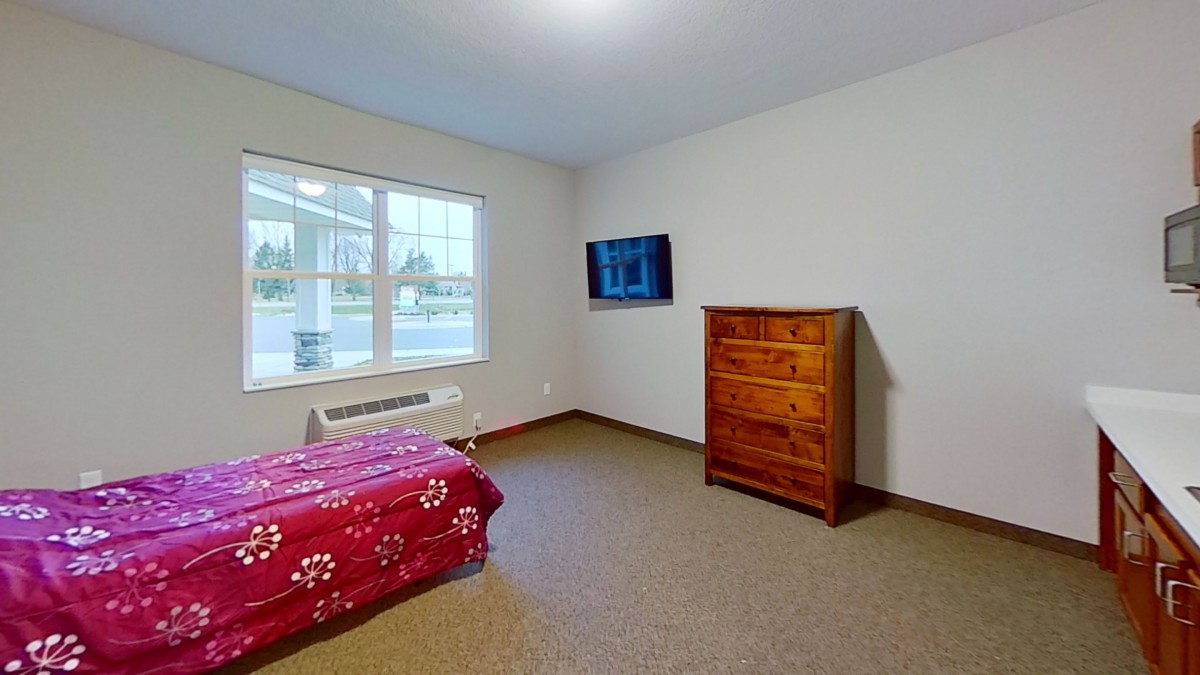 A simple bedroom with a bed, dresser, wall-mounted TV, and window.