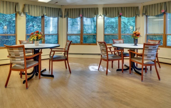 A cozy dining area with round tables and wooden chairs near large windows.