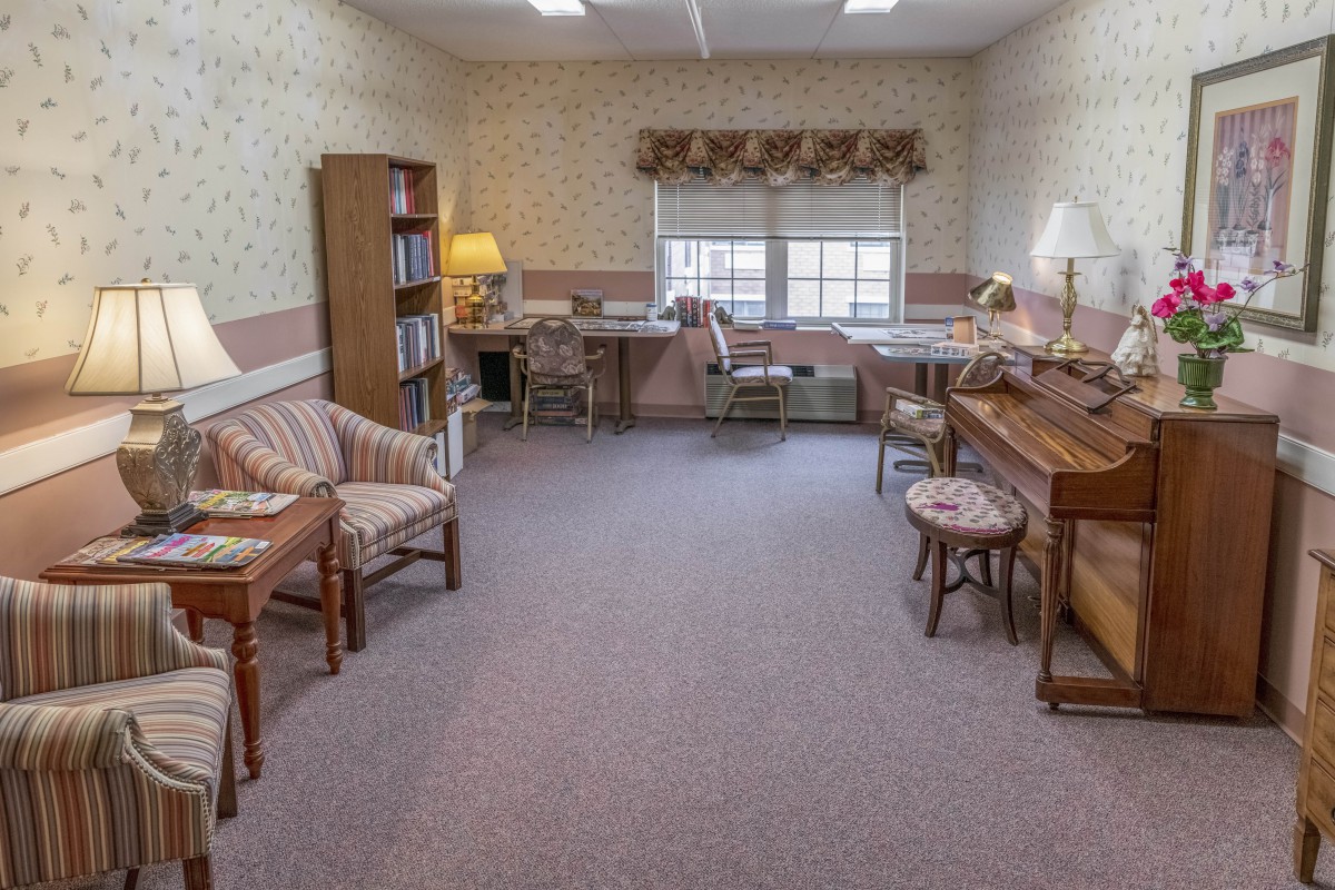A cozy office space featuring a piano, desk, bookshelf, and seating area.