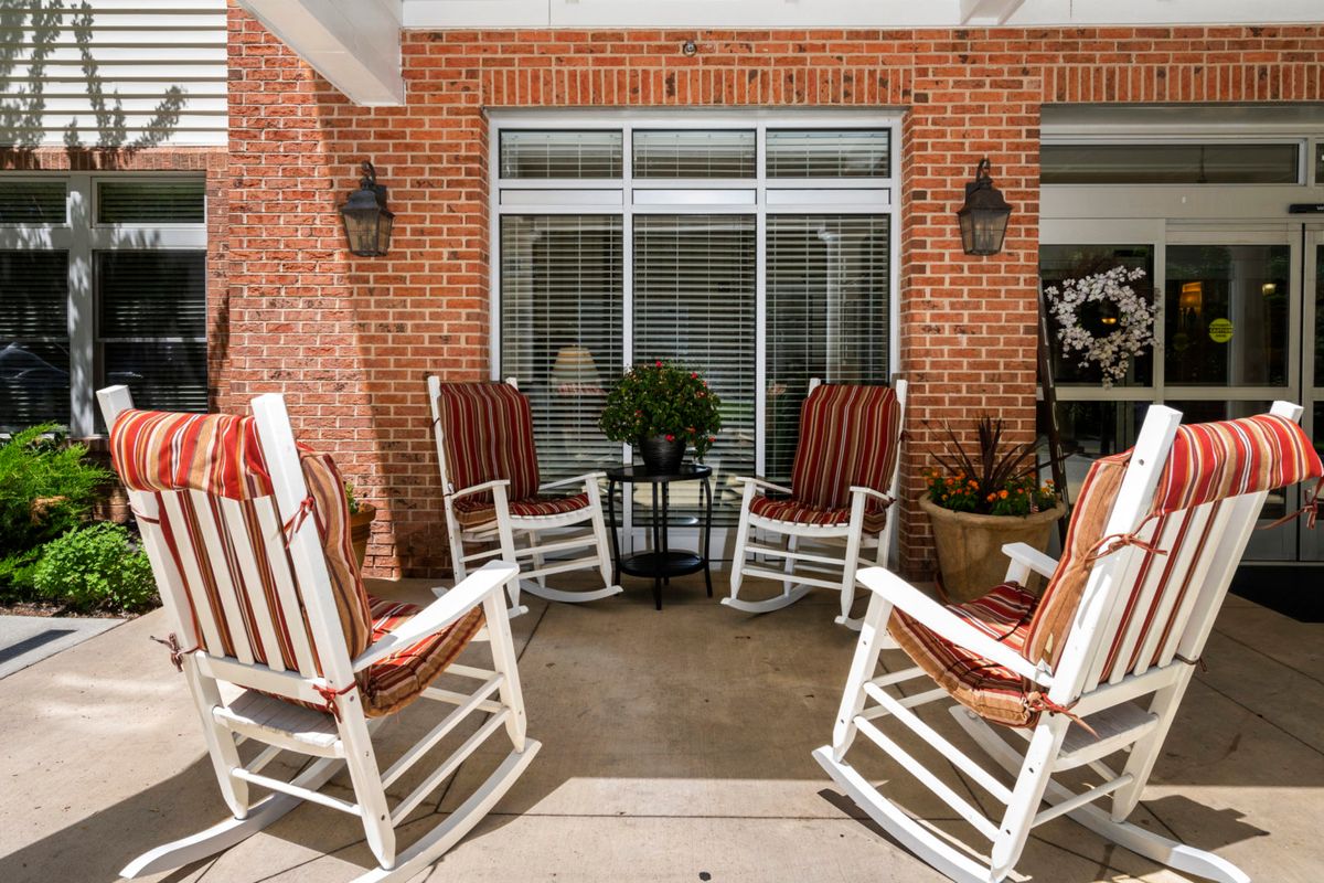 A cozy porch with white rocking chairs arranged around a small table in front of a brick wall.