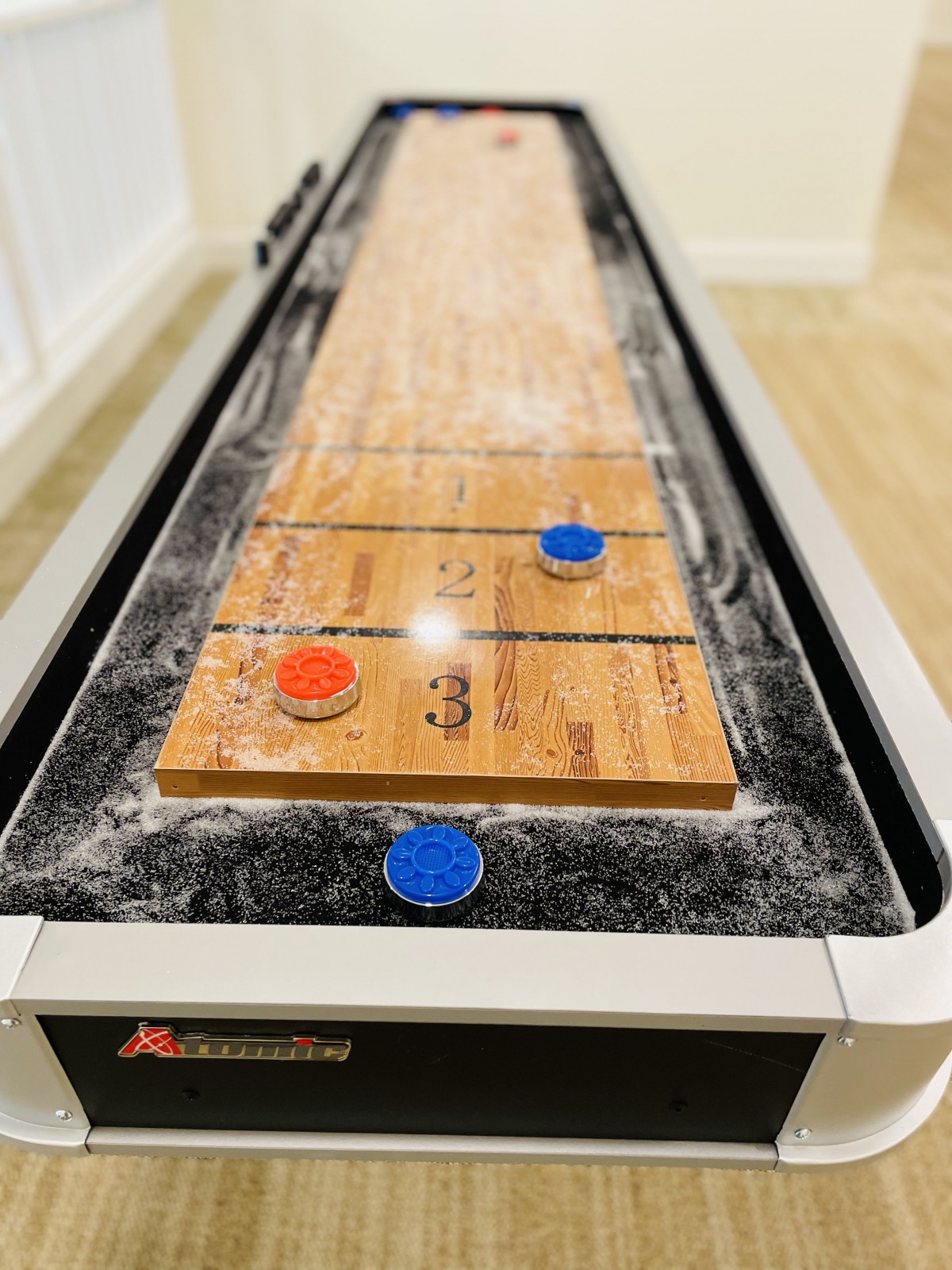 A shuffleboard table with red and blue pucks positioned on the board.