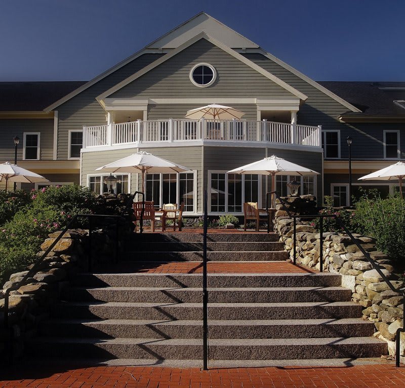 A two-story building with a patio and umbrellas, viewed from the front steps.