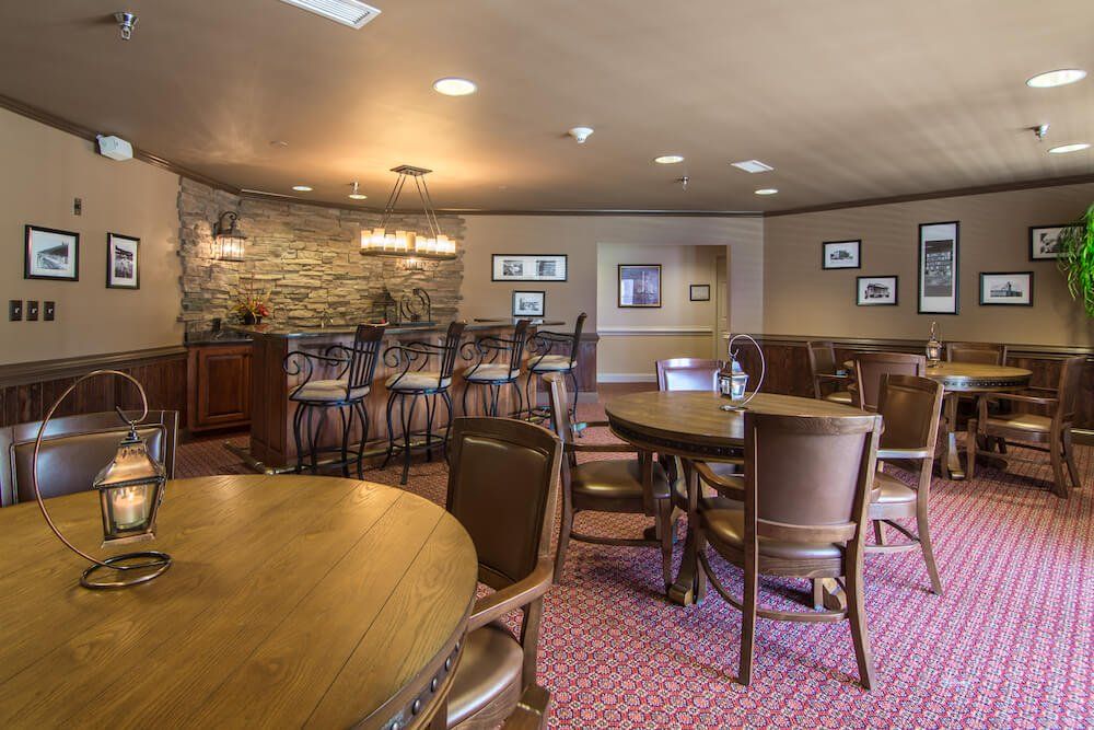 A cozy dining area featuring wooden tables and chairs, with a bar counter in the background and warm lighting.