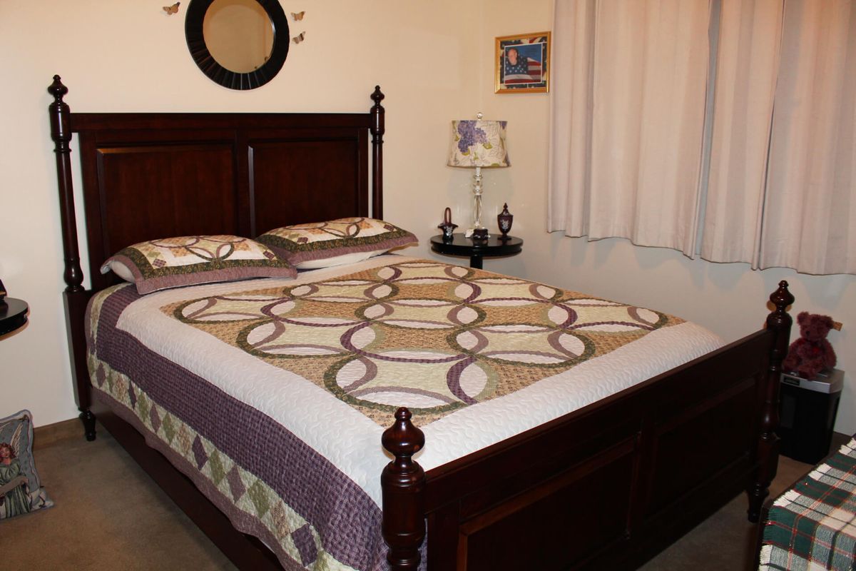 A cozy bedroom with a wooden bed frame, decorative quilt, and bedside lamp.