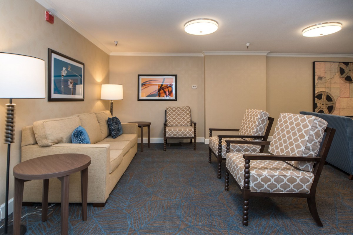A well-lit waiting room with comfortable seating arrangements, including a sofa and armchairs, complemented by wall art and a lamp.