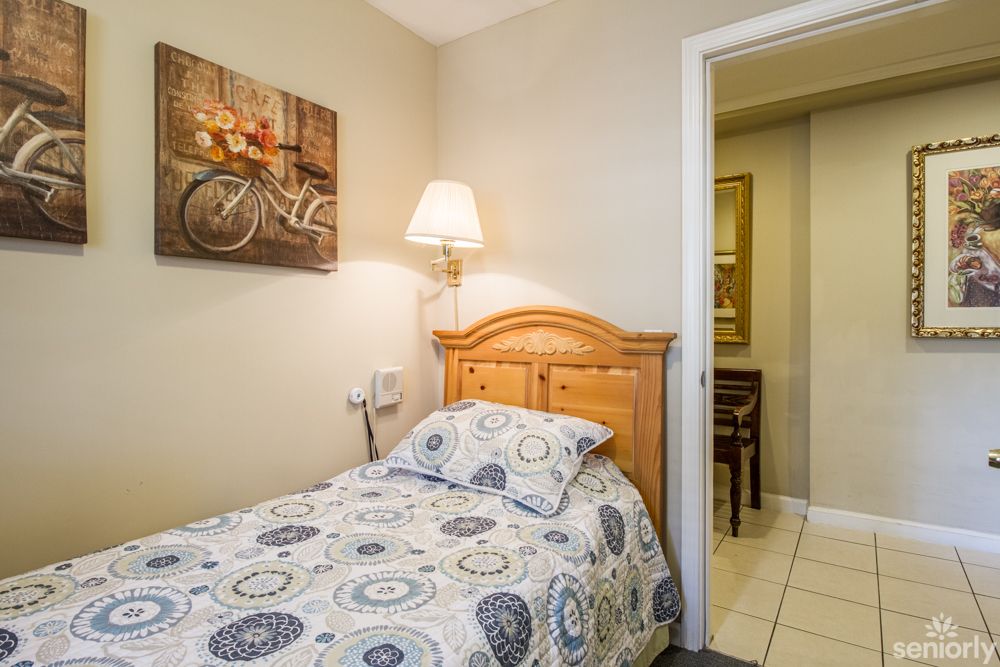A cozy bedroom featuring a single bed with patterned bedding, decorated with a bicycle-themed wall art and illuminated by a wall-mounted lamp.