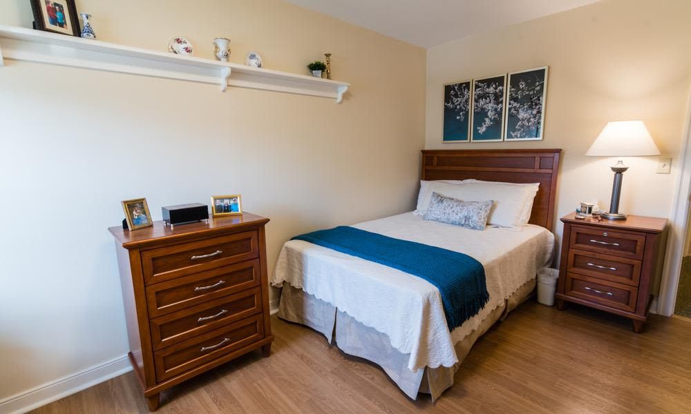 A neatly arranged bedroom with a bed, wooden dresser, and decorative wall art.