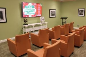 A modern conference room with orange chairs and a large TV screen for presentations.