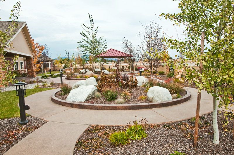 A scenic garden with a circular pathway surrounding a pavilion, featuring various plants and rocks.