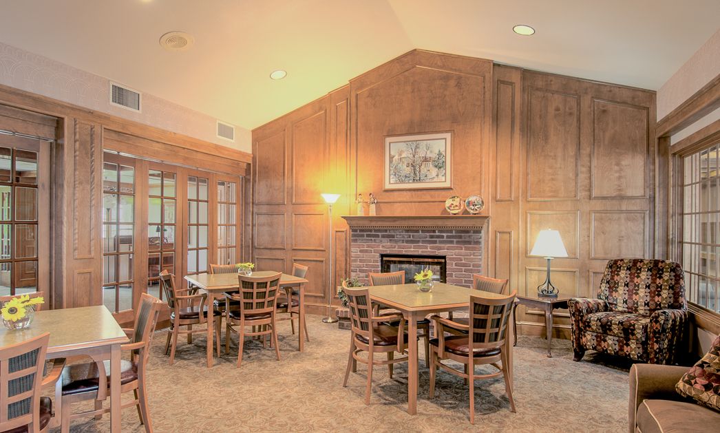 A cozy dining area with wood paneling, featuring tables and chairs arranged around a central fireplace.