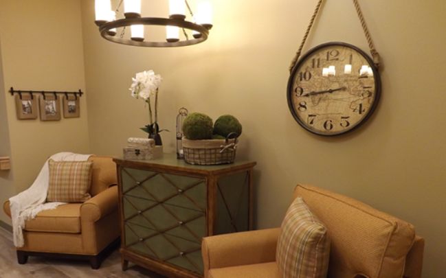 A cozy living room with elegant decor, featuring a wall clock, chandelier, and comfortable armchairs.