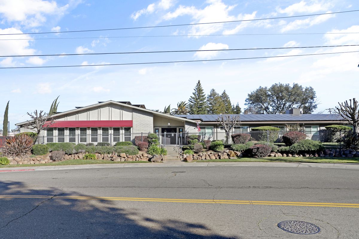 A roadside building with a red awning, trees in the background, and a clear blue sky.