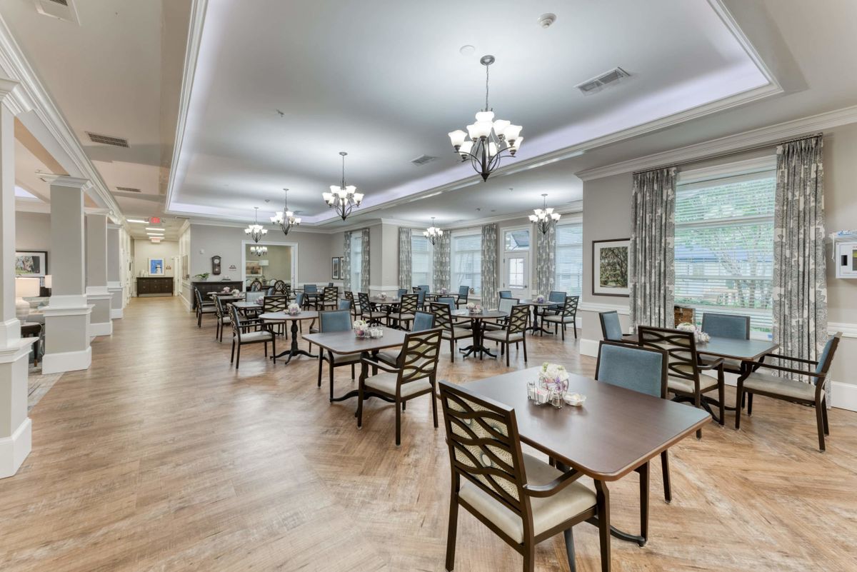 A spacious and elegantly decorated dining room with neatly arranged tables and chairs, featuring large windows and stylish lighting.