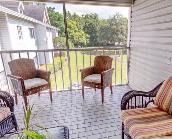 A cozy screened balcony with comfortable chairs overlooking a lush green garden.