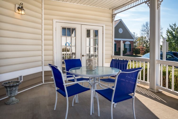 A cozy patio setup with a glass table and blue chairs on a sunny porch.