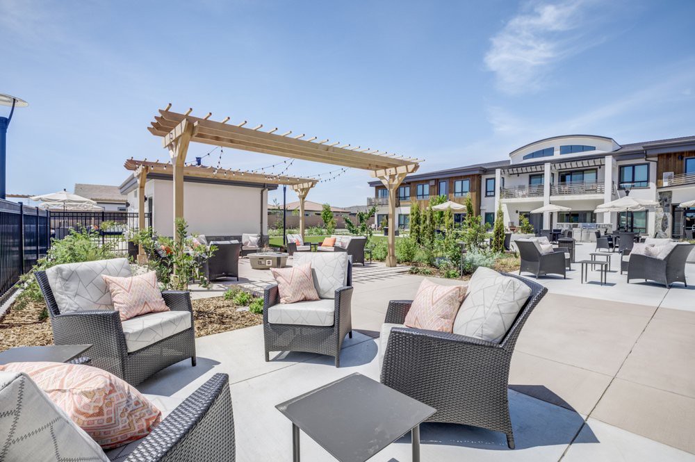 A modern outdoor patio area with comfortable seating and a wooden pergola in an apartment complex.