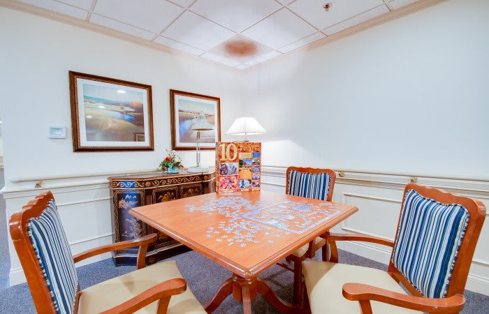 A cozy room with a table set for puzzle assembly, surrounded by chairs and adorned with artwork.