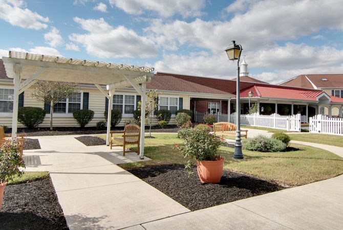A charming building with a well-maintained garden area, featuring benches and a lamp post under a partly cloudy sky.