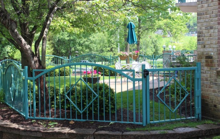 A lush garden area enclosed by a teal metal fence, with trees and plants providing a serene outdoor setting.