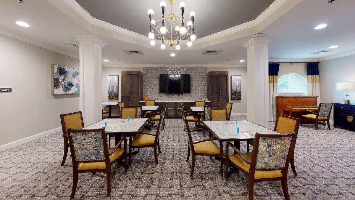 A modern dining area with neatly arranged tables and chairs, featuring a stylish chandelier and a mounted television.