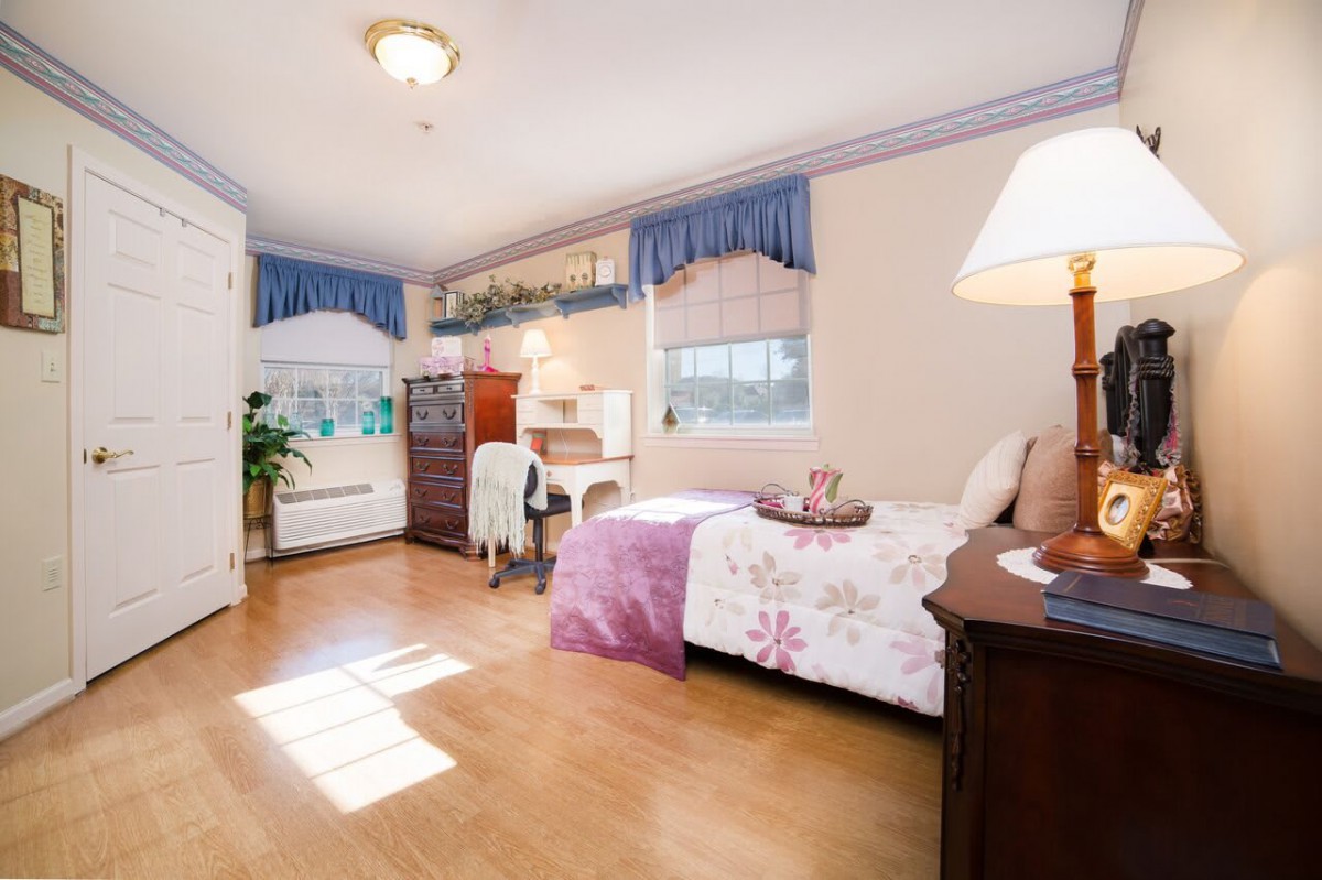 A cozy bedroom with natural light, featuring a bed, desk, and elegant furnishings.