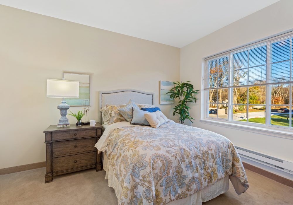 A cozy bedroom with a neatly made bed, nightstand, and a large window.