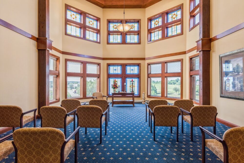A well-lit meeting room with multiple chairs arranged on a blue carpet and large windows with wooden frames.