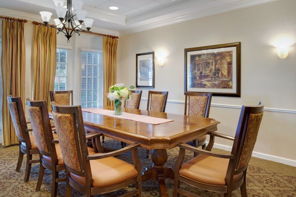 A well-furnished dining room featuring a large wooden table surrounded by chairs, with artwork on the walls and a chandelier above.