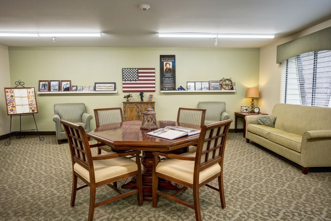 A well-furnished office meeting room featuring a wooden table, chairs, a sofa, and an American flag on the wall.