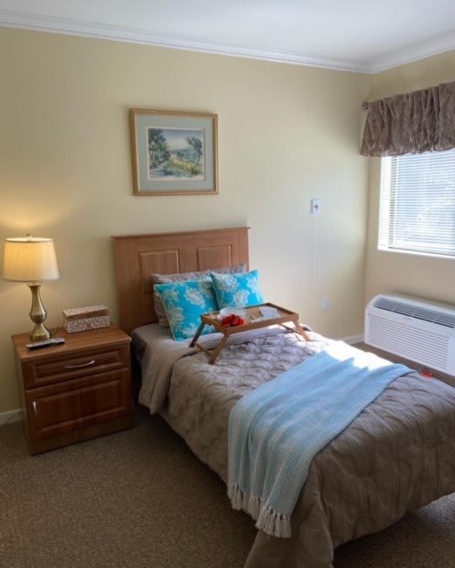 A cozy bedroom with a single bed, nightstand, and a window letting in natural light.