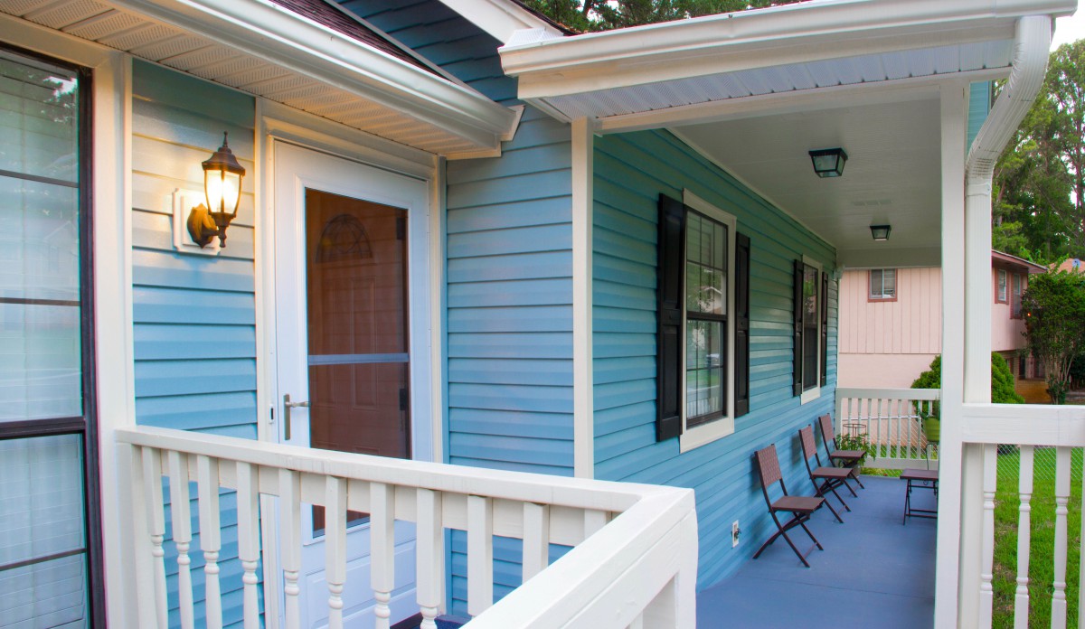 A cozy porch with blue siding, featuring a railing and two chairs.