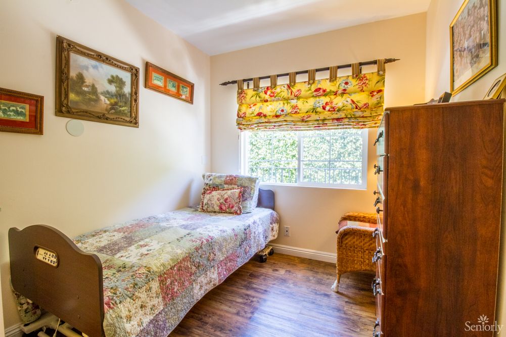 A small, cozy bedroom with a single bed, decorated with colorful curtains and a wooden floor.