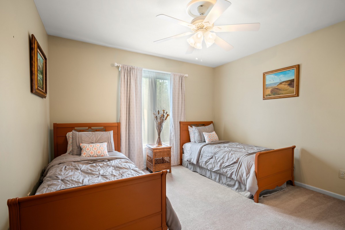 A cozy bedroom with two twin beds, carpeted floor, and a ceiling fan.