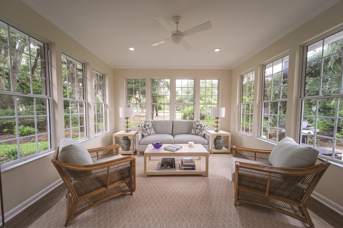 A cozy sunroom with abundant natural light, featuring comfortable seating and large windows.